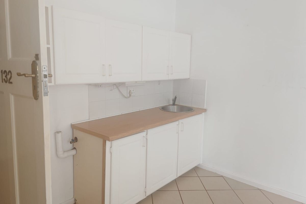 A compact, empty kitchen area featuring white built-in cabinetry, a laminate countertop, a stainless steel sink, and tiled flooring.