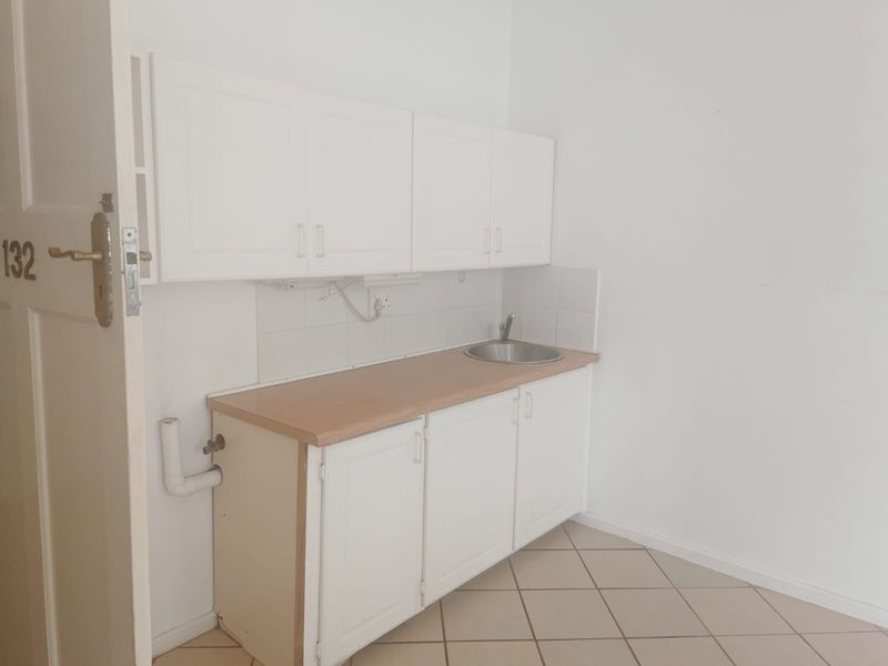 A compact, empty kitchen area featuring white built-in cabinetry, a laminate countertop, a stainless steel sink, and tiled flooring.