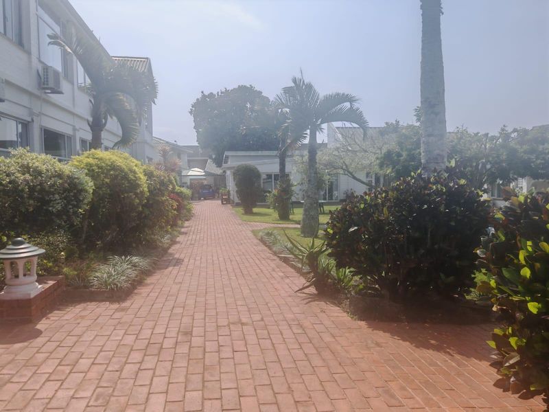 A well-maintained brick paved pathway leading through a landscaped garden area between apartment building wings.