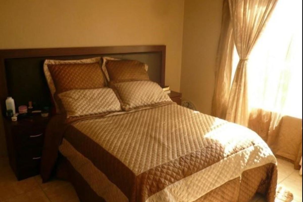 A bedroom featuring tiled flooring and a built-in headboard, illuminated by natural light through the window.