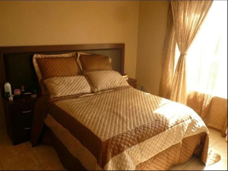 A bedroom featuring tiled flooring and a built-in headboard, illuminated by natural light through the window.