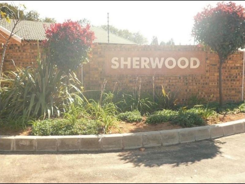 Entrance view of the Sherwood complex featuring a brick boundary wall, electric fencing, and landscaped garden area.