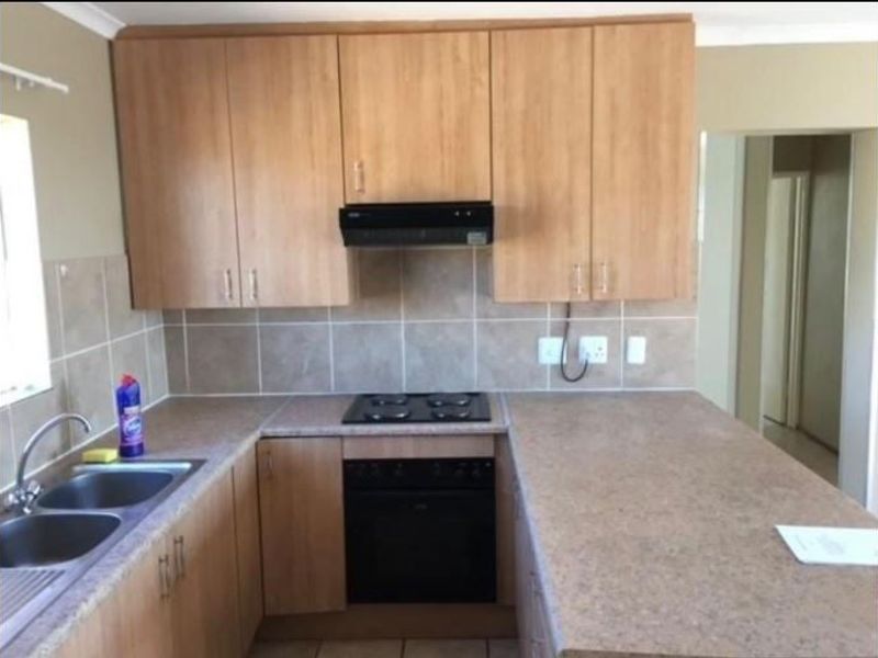 A functional kitchen featuring light wood-look cabinetry, laminate countertops, a built-in oven with hob, and a tiled backsplash.