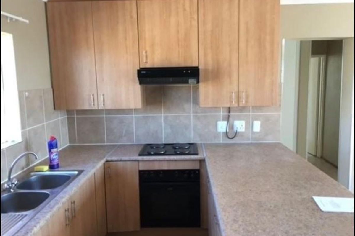 A functional kitchen featuring light wood-look cabinetry, laminate countertops, a built-in oven with hob, and a tiled backsplash.