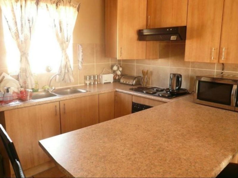 Functional kitchen featuring laminate cabinetry, laminate countertops, a double bowl sink, and built-in cooking appliances with a tiled backsplash.