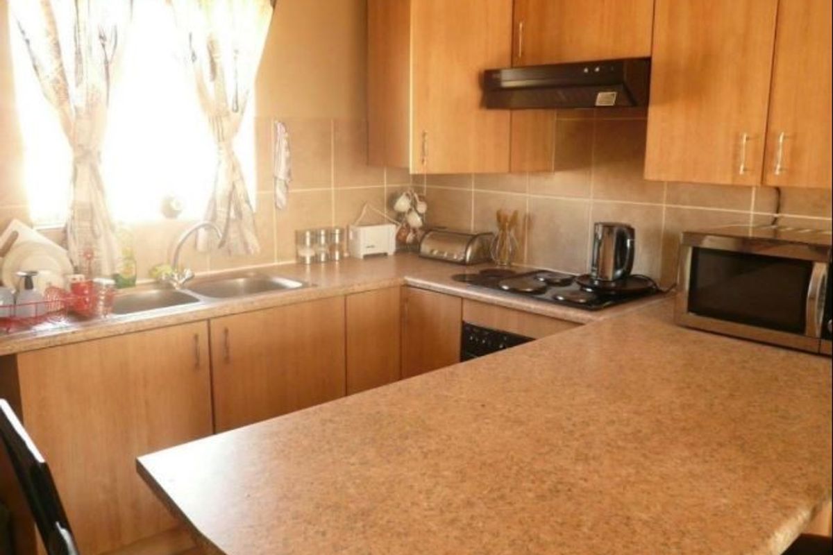Functional kitchen featuring laminate cabinetry, laminate countertops, a double bowl sink, and built-in cooking appliances with a tiled backsplash.