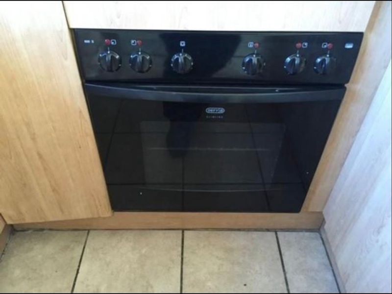 A close-up view of a built-in black oven integrated into light wood-finish kitchen cabinetry with tiled flooring.