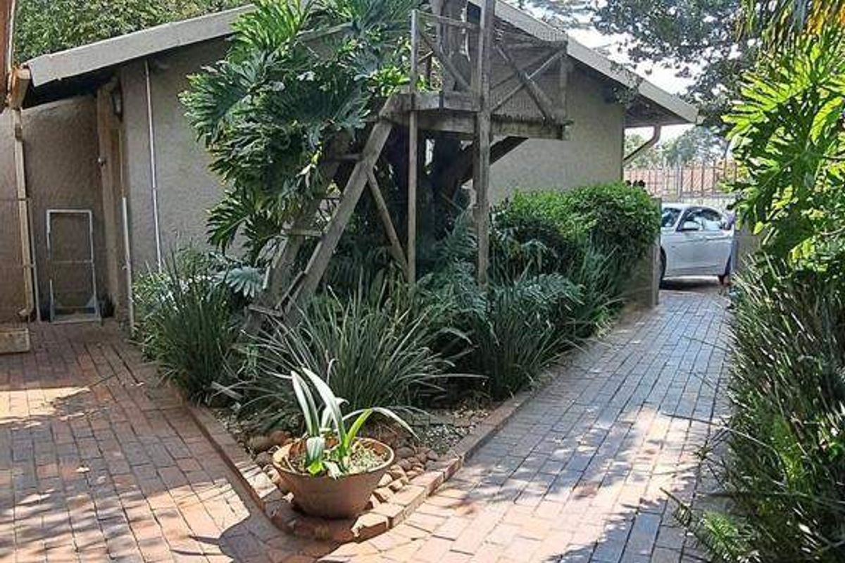A rear garden area featuring brick paved pathways, mature landscaping, and a wooden treehouse structure.