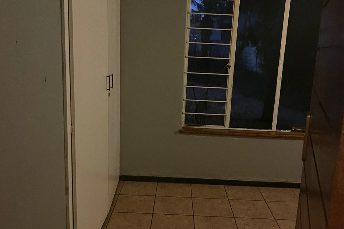 An empty bedroom featuring tiled flooring, built-in cupboards, exposed ceiling beams, and security bars on the window.