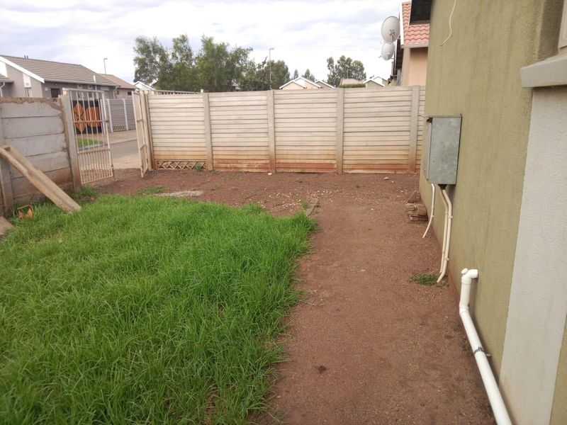 A rear garden area featuring a precast concrete boundary wall, metal gate, and exposed external utility infrastructure.