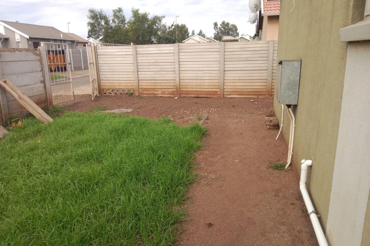 A rear garden area featuring a precast concrete boundary wall, metal gate, and exposed external utility infrastructure.