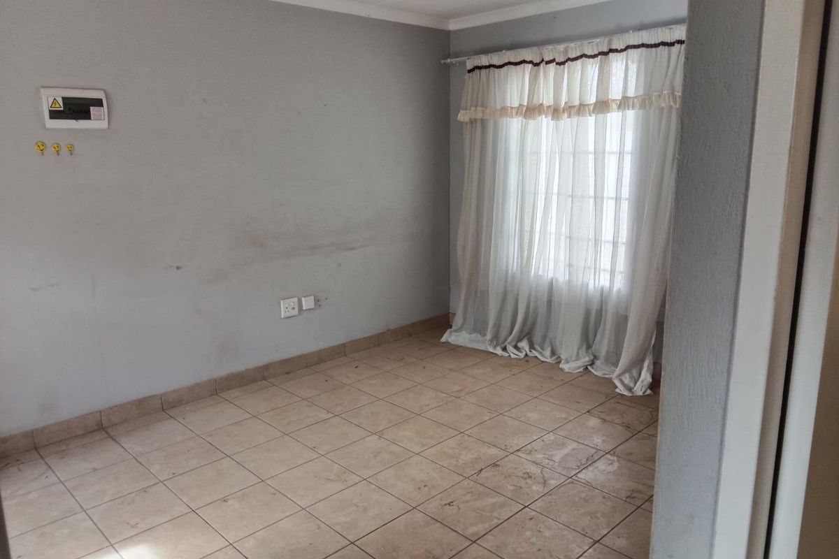 An empty bedroom featuring tiled flooring, a wall-mounted electrical distribution board, and a window with a curtain rail.