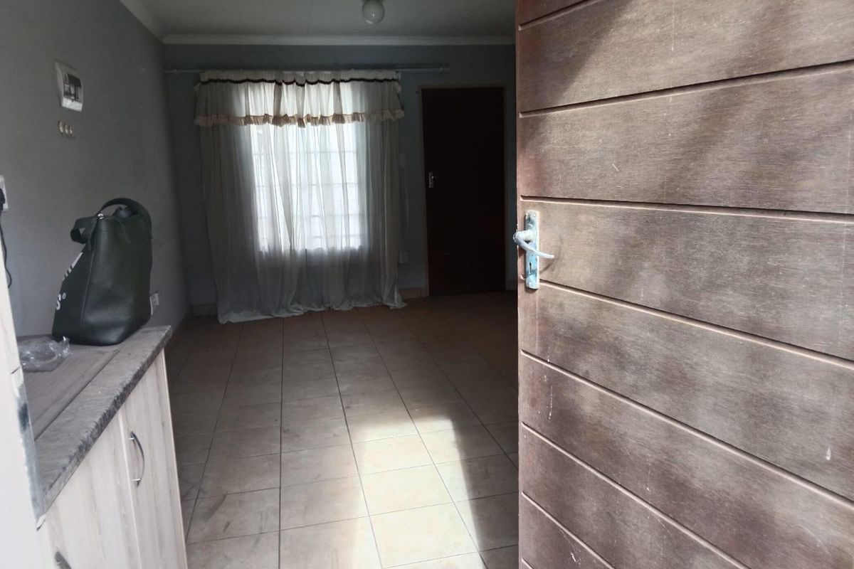 An empty living room featuring tiled flooring and a wooden entrance door, offering a blank canvas for interior design.