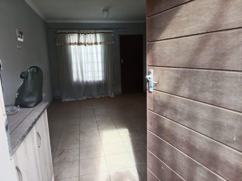 An empty living room featuring tiled flooring and a wooden entrance door, offering a blank canvas for interior design.