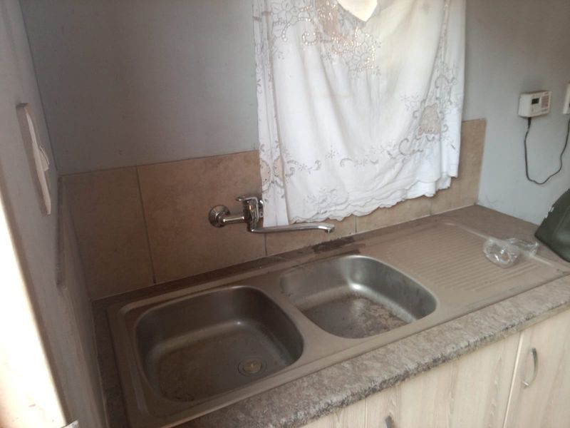 A functional kitchen sink area featuring a double bowl stainless steel sink, wall-mounted tap, and tiled splashback with laminate cabinetry.