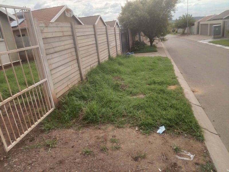 A street-level view showing the property boundary, precast concrete wall, metal gate, and the adjacent road and grass verge.