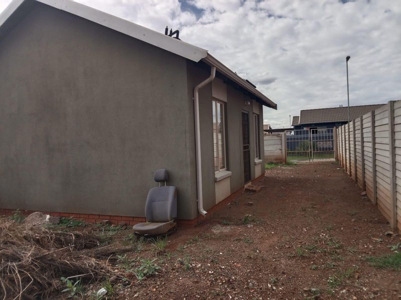 A view of the rear exterior of the house featuring a plain rendered facade, guttering, and a precast concrete boundary wall.