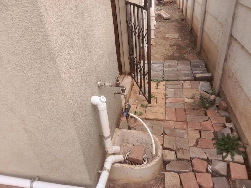 A narrow side exterior area featuring a utility sink, external tap, paved walkway, and security gate access.