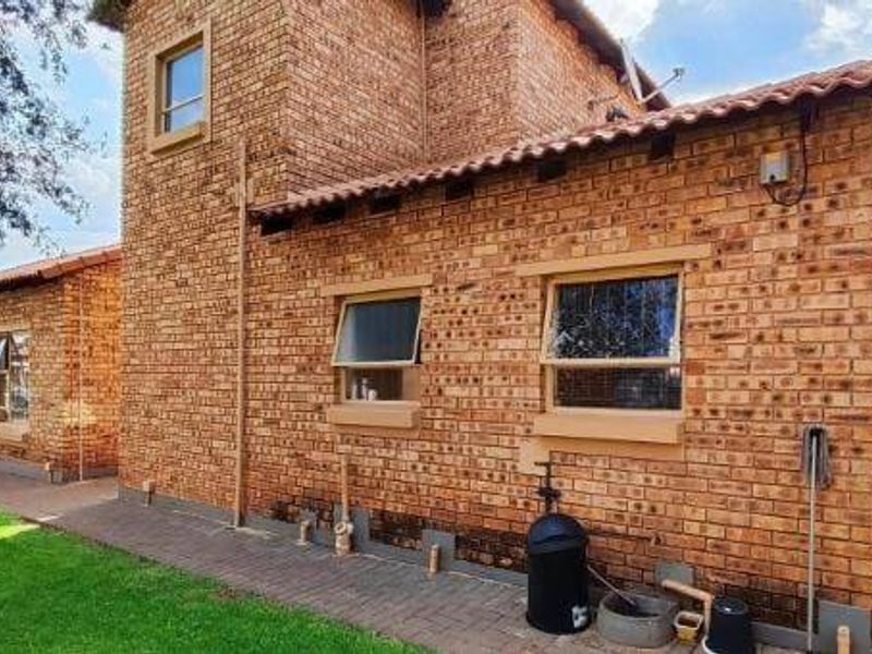 A view of the rear exterior of the townhouse, featuring face-brick construction, terracotta roof tiles, and a paved walkway alongside a well-maintained lawn.