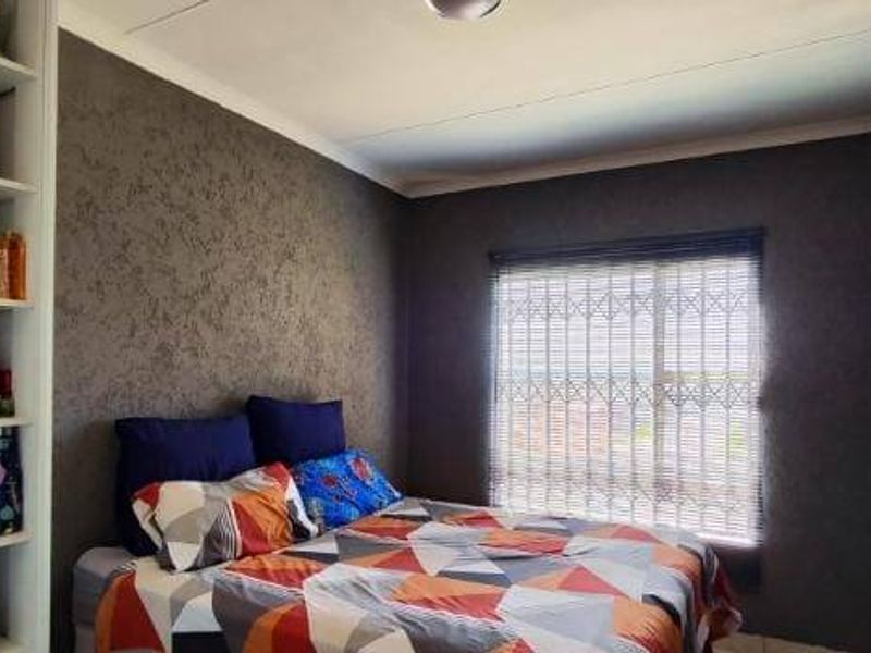 A bedroom featuring dark textured walls, built-in shelving units, and a window fitted with a security gate and blinds.