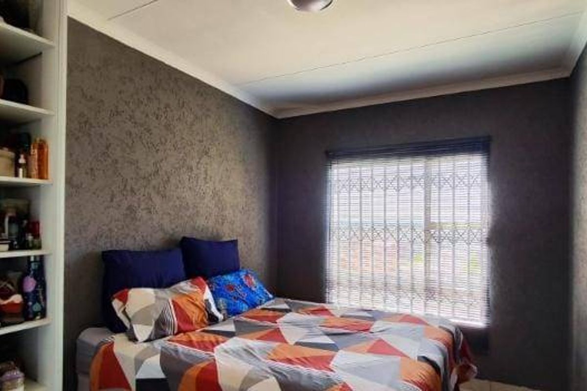 A bedroom featuring dark textured walls, built-in shelving units, and a window fitted with a security gate and blinds.