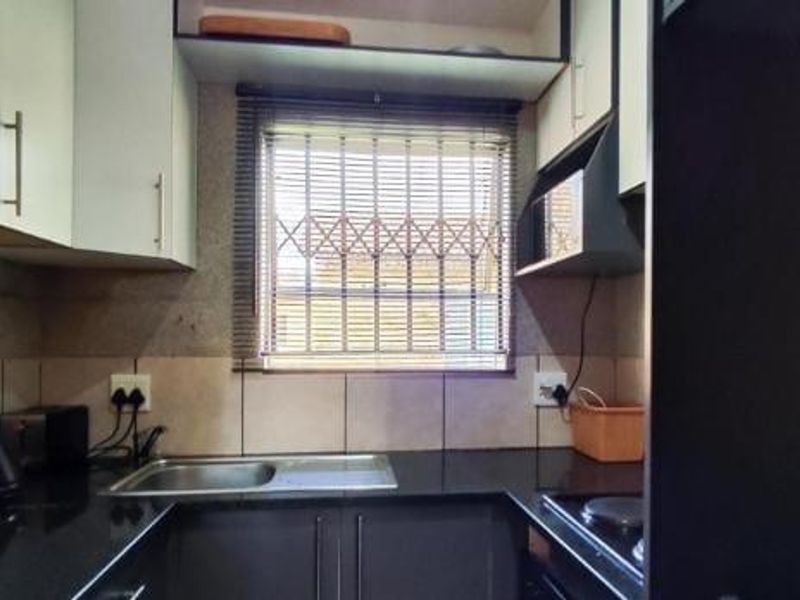 Compact kitchen featuring modern dark cabinetry, granite countertops, stainless steel sink, and a window with security bars for added safety.