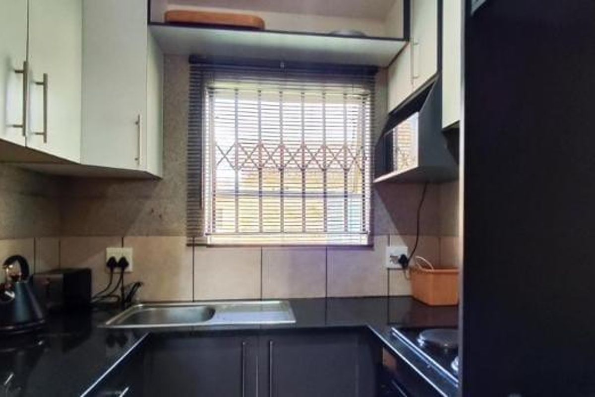 Compact kitchen featuring modern dark cabinetry, granite countertops, stainless steel sink, and a window with security bars for added safety.
