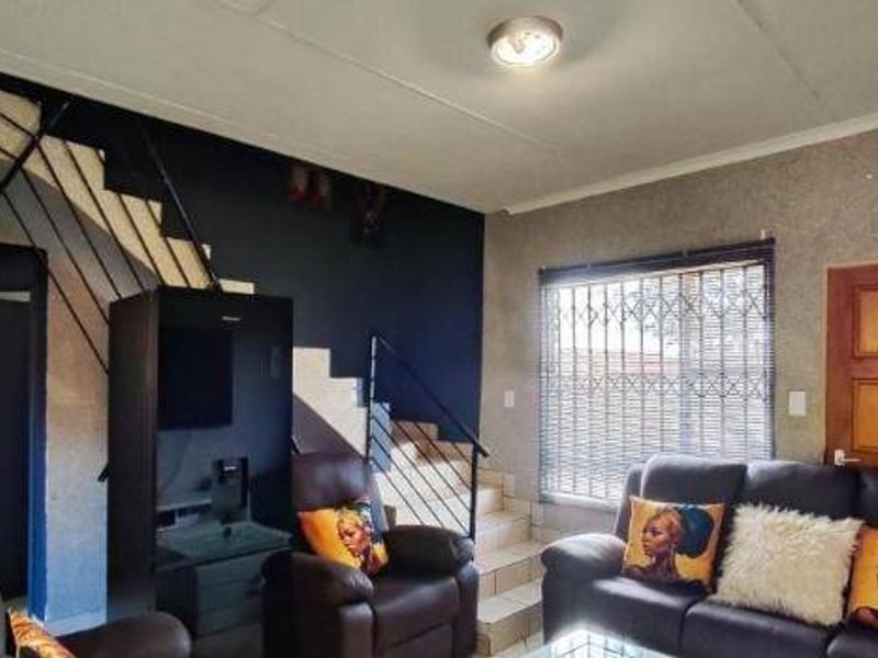 A living room featuring a staircase with a metal balustrade, security gate on the window, and tiled flooring.