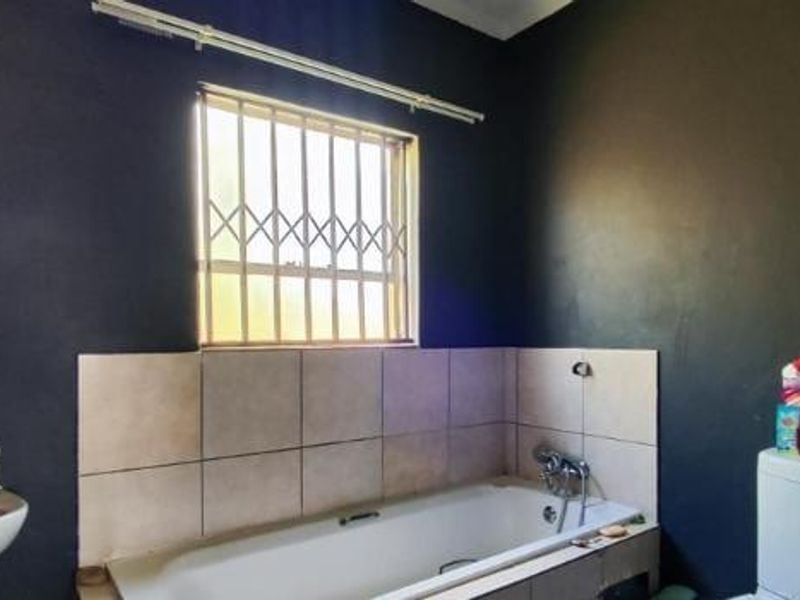 A bathroom featuring a bathtub with tiled splashback, pedestal sink, and security bars on the window. The walls require cosmetic attention.