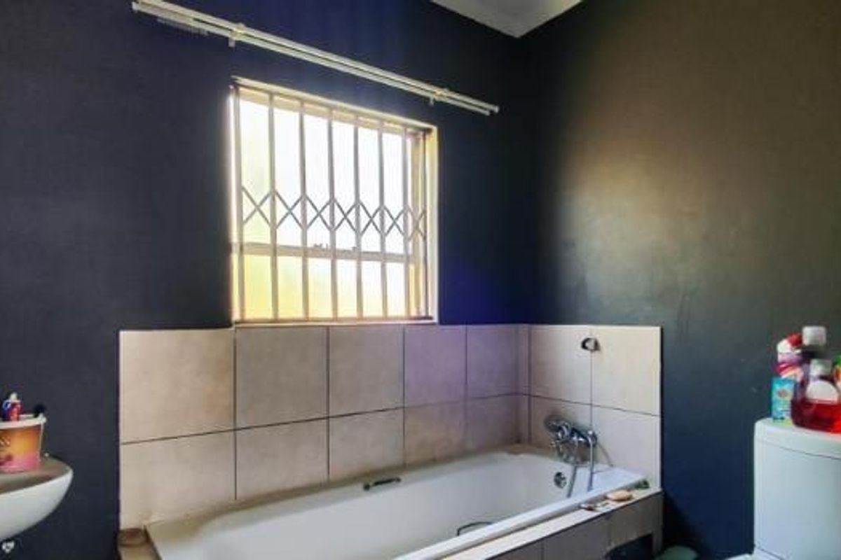 A bathroom featuring a bathtub with tiled splashback, pedestal sink, and security bars on the window. The walls require cosmetic attention.