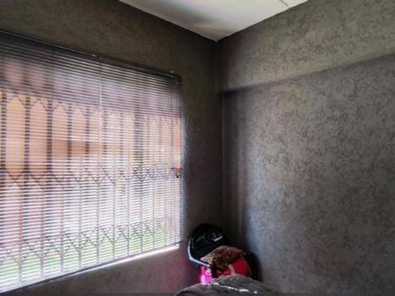 A bedroom featuring textured walls, a window with venetian blinds, and an integrated security gate.