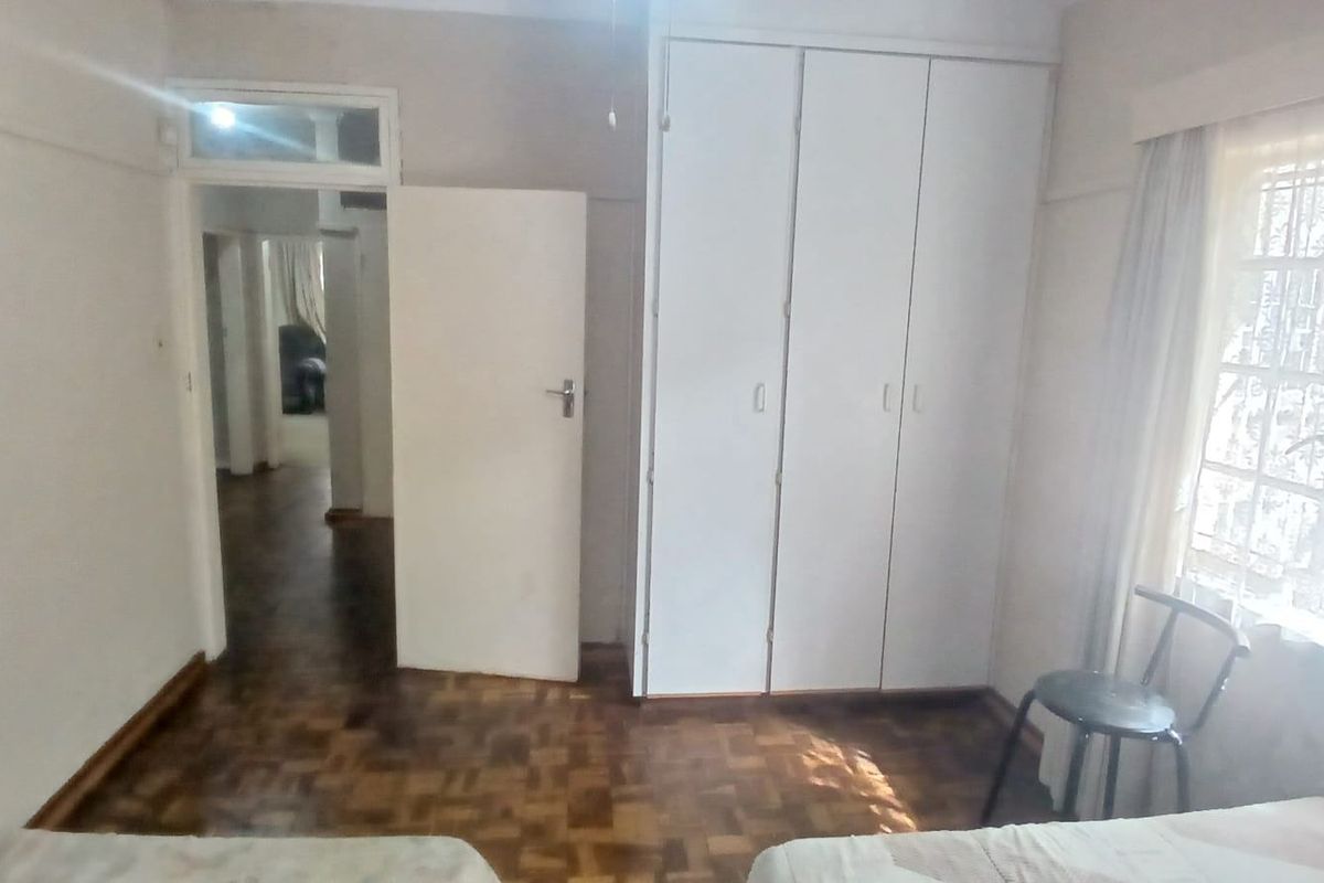 A bedroom featuring classic parquet flooring, built-in cupboards, and a window with natural light, offering a functional space with potential for cosmetic updates.