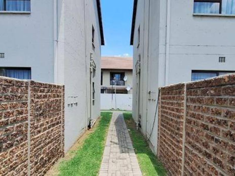 A view of the exterior walkway between apartment blocks, featuring brick boundary walls, a paved path, and grass landscaping.
