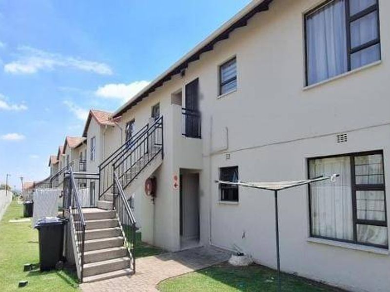 Rear view of a multi-story apartment complex featuring external staircases, paved walkways, and aluminium window frames.