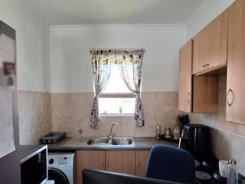 Compact kitchen featuring laminate cabinetry, tiled splashbacks, and a stainless steel sink with a window view.