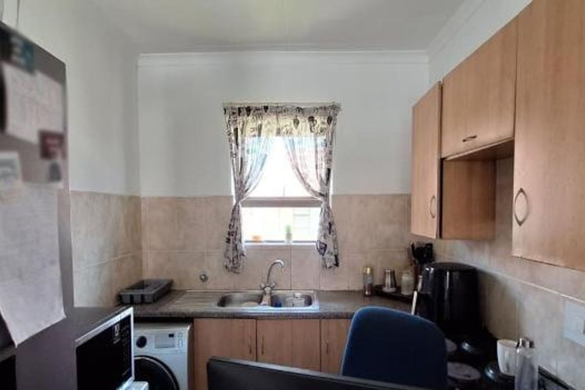 Compact kitchen featuring laminate cabinetry, tiled splashbacks, and a stainless steel sink with a window view.