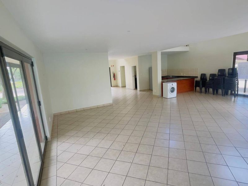 Spacious open-plan living area featuring tiled flooring, neutral walls, and a functional kitchen counter, offering a versatile layout for various living arrangements.
