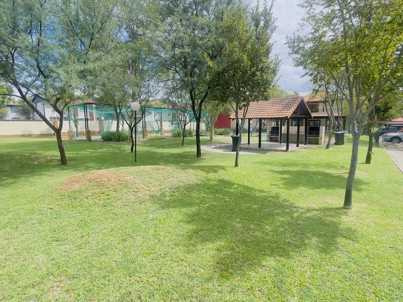 A well-maintained communal garden area featuring mature trees, a manicured lawn, and a covered gazebo with built-in braai facilities.