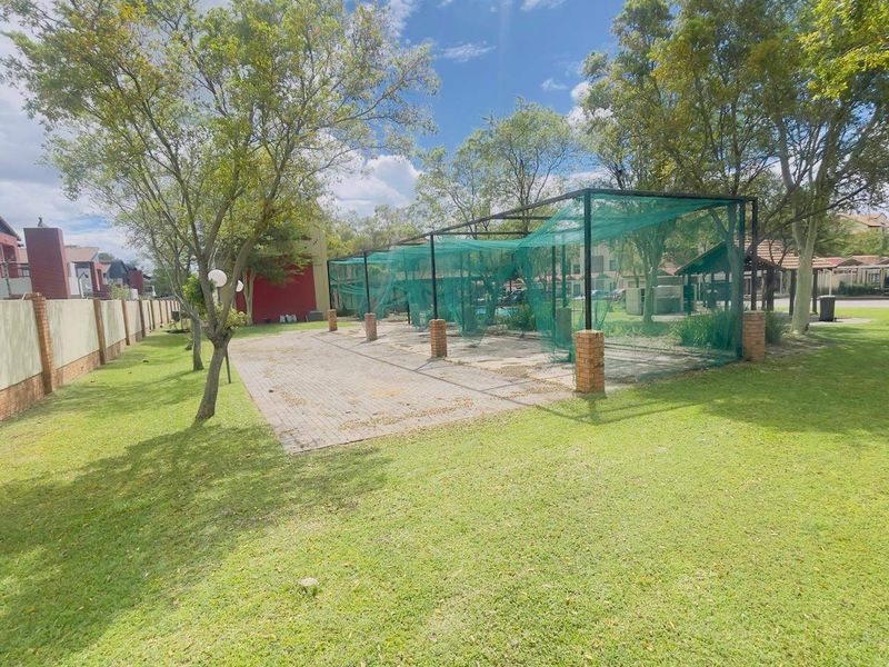 Outdoor sports facility featuring a paved cricket practice area with fixed netting, brick support pillars, and surrounding landscaped lawn.