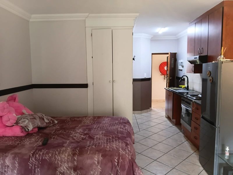 Open-plan studio apartment featuring a compact kitchenette with built-in cabinetry, tiled flooring, and integrated storage cupboards.
