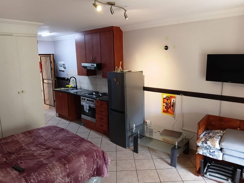 Open-plan studio apartment featuring a compact kitchenette with built-in cabinetry, electric stove, and tiled flooring throughout.