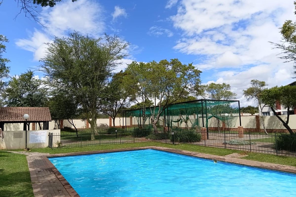 Communal swimming pool area featuring a paved surround, covered gazebo, and landscaped garden within a secure fenced perimeter.