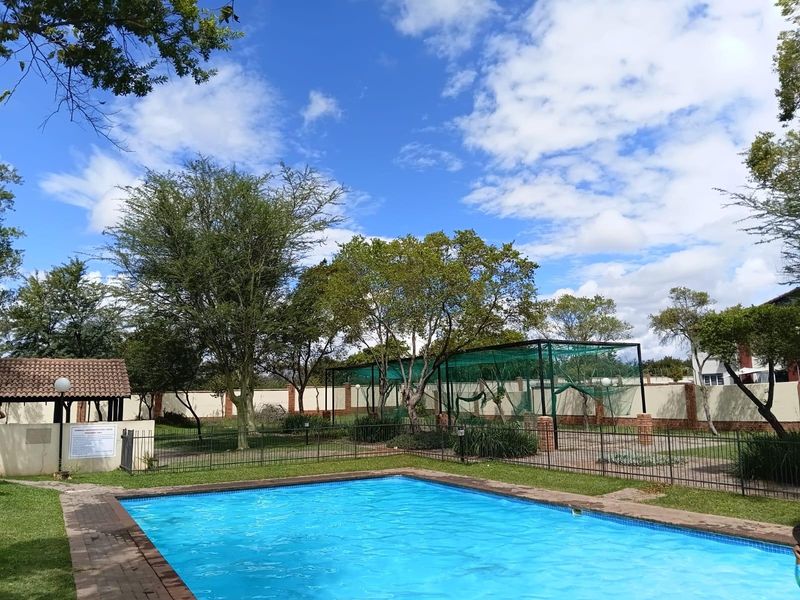 Communal outdoor area featuring a swimming pool, paved surrounds, and a sports practice net enclosure within a secure boundary wall setting.
