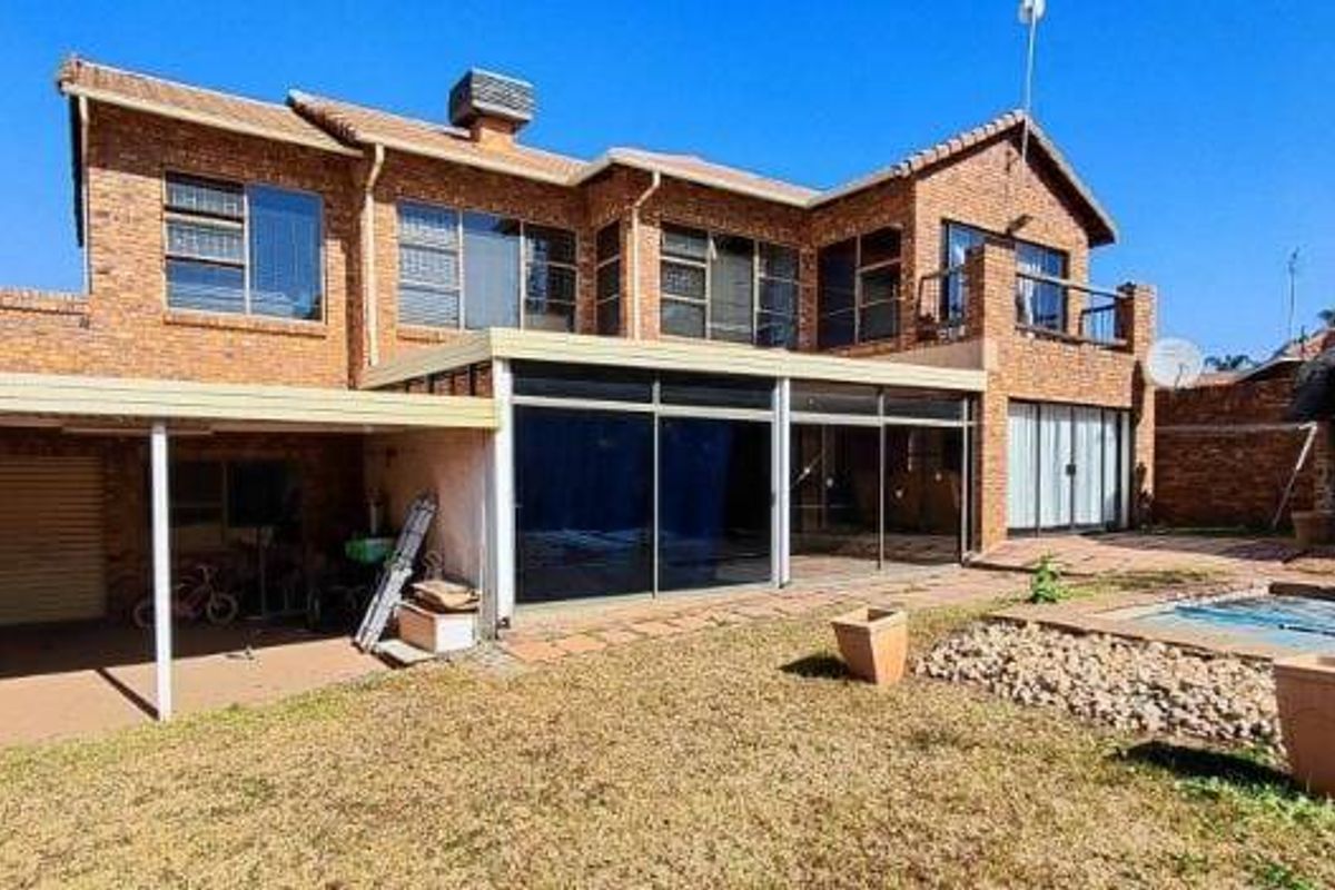 Rear view of a double-story face brick house featuring a covered patio, swimming pool, and a separate lapa area in the garden.