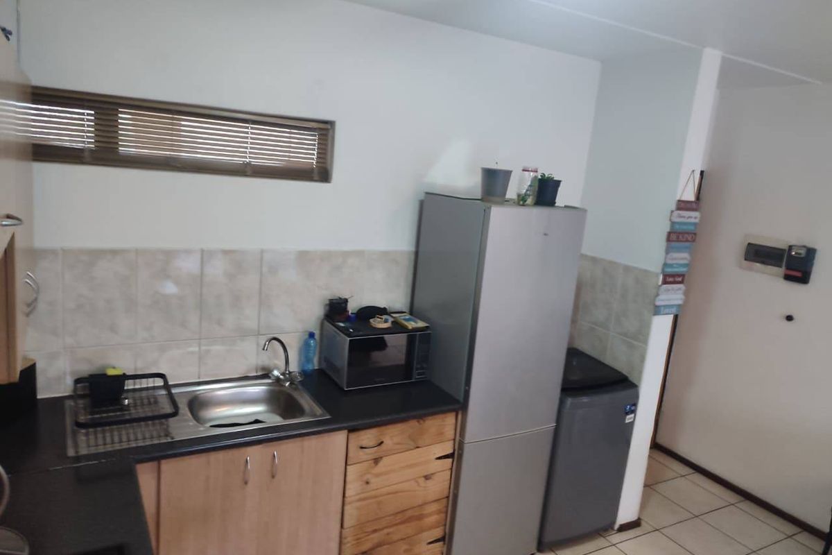 A functional kitchen area featuring laminate countertops, a stainless steel sink, tiled backsplash, and built-in cabinetry with tiled flooring.