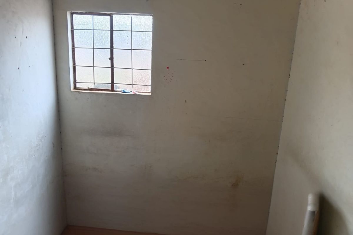 A small, vacant room featuring a window with security bars and laminate flooring, requiring cosmetic updates and wall repairs.