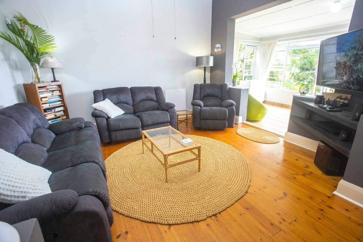 Spacious living room featuring polished timber flooring and an open-plan layout connecting to an adjacent sunroom area with large windows.