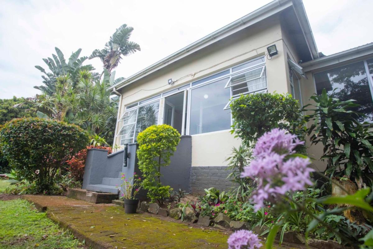 Rear view of the property featuring a paved walkway, landscaped garden, and access to the home through a glass-paneled entrance.