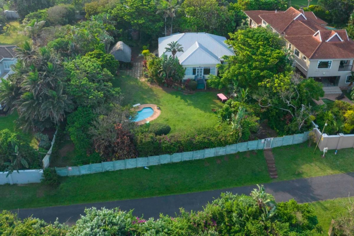 Aerial view of a residential property featuring a spacious garden, a swimming pool, and a detached structure, surrounded by mature trees and greenery.