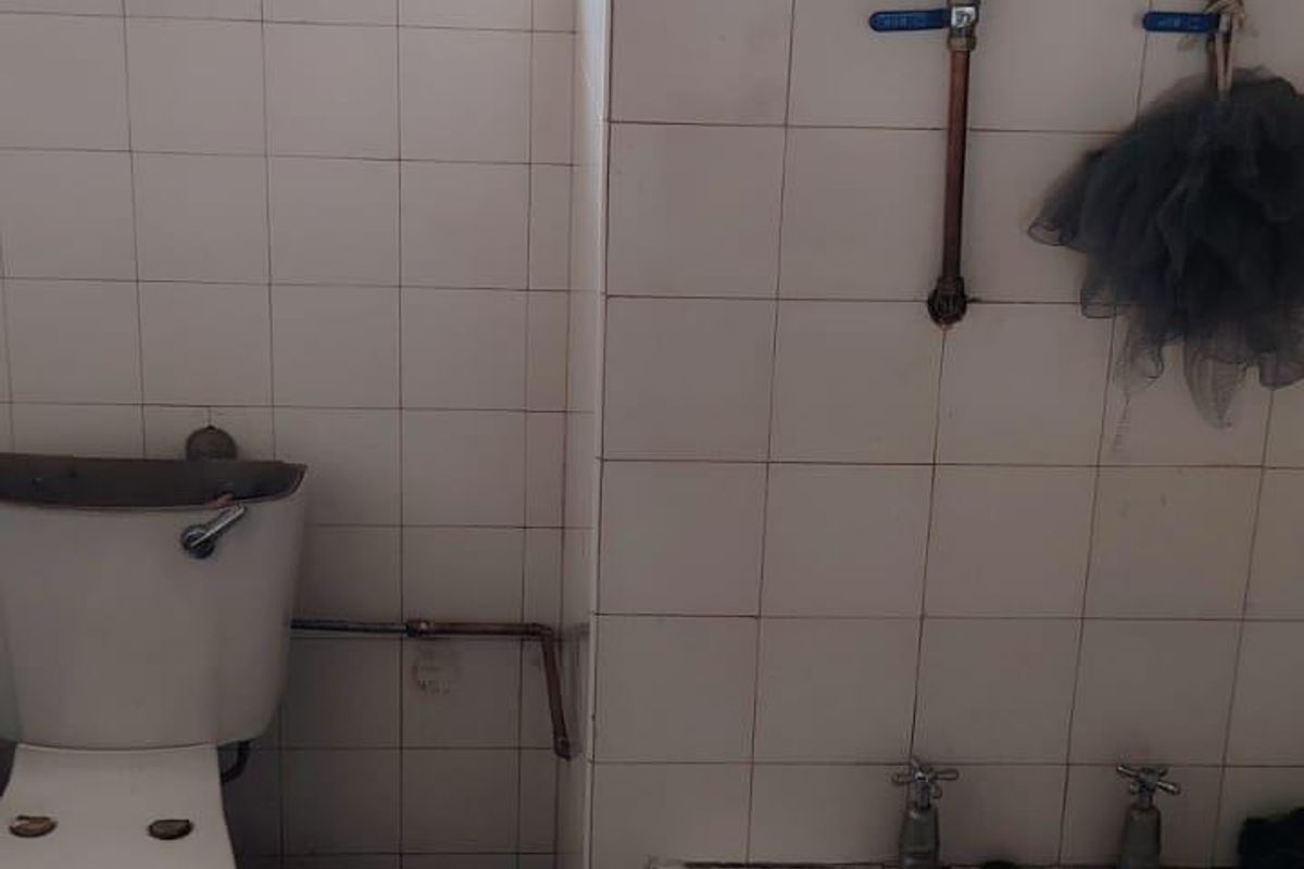 A dated bathroom featuring a standard bathtub and toilet with exposed plumbing and tiled walls, requiring significant renovation and modernization.